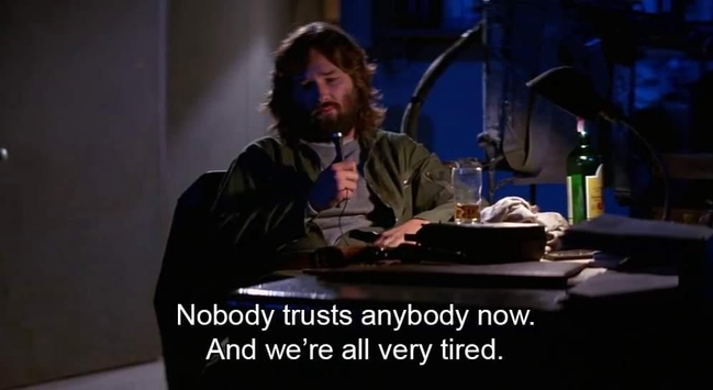 The movie protagonist is sitting at dimly lit desk with a nearly empty glass of hard liquor, visibly exhausted and with an expression of despair and exasperation on his face.
The protagonist speaks into a dictaphone's microphone, saying: "Nobody trusts anybody now. And we're all very tired."