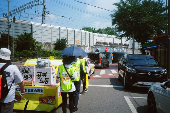 택시 모형을 끌고 가는 행진대오가 굴다리 아래를 마주하고 있다.
