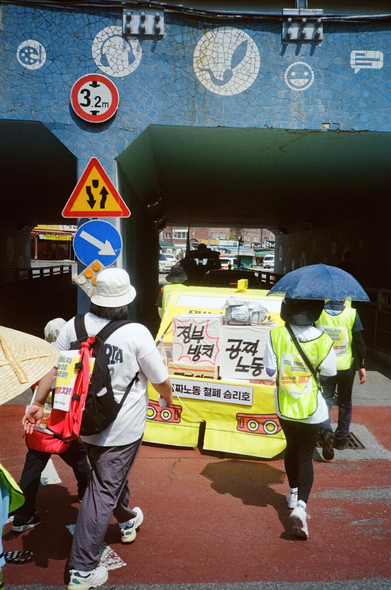 굴다리 아래로 걸어들어가는 행진 대오와 택시 모형.